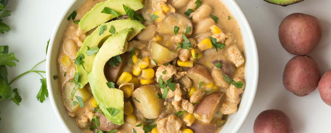 A bowl of white chili with chicken and beans and avocado.