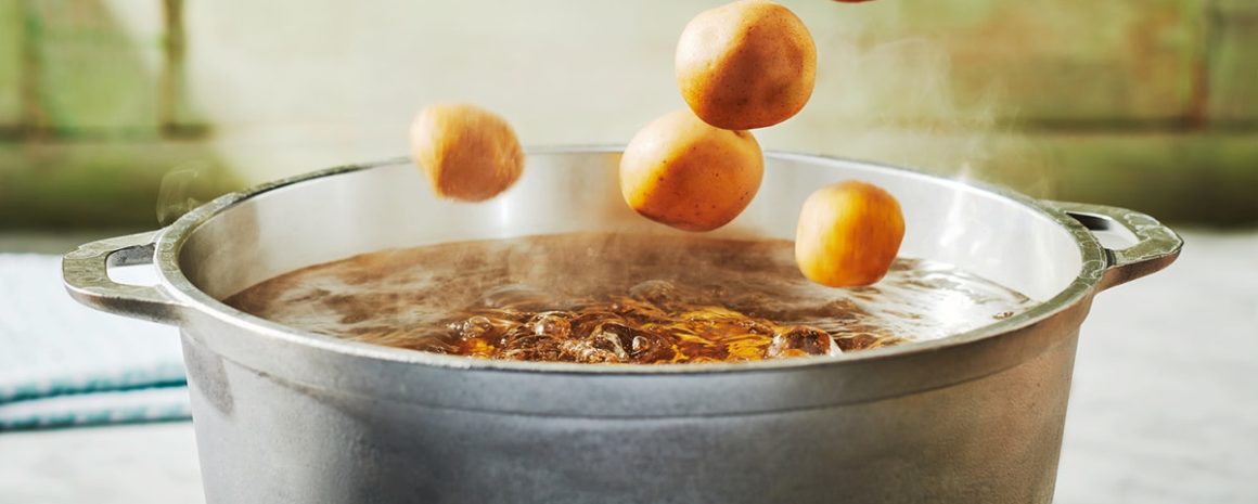 Potatoes being tossed into a pot of boiling water.