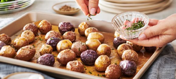 A tray of little potatoes with herbs being sprinkled on.