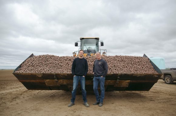Two of our farmers standing in front of a giant tractor of potatoes.